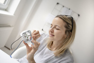 Portrait of a smiling young woman holding camera at home