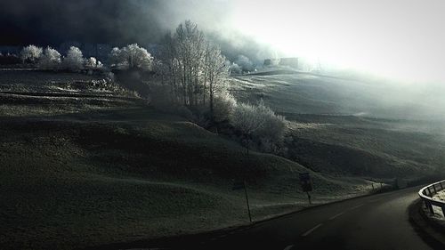 Road by snow covered landscape against sky