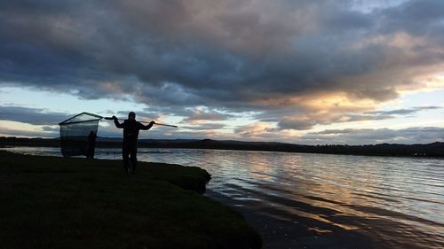 Silhouette of man standing on beach against cloudy sky