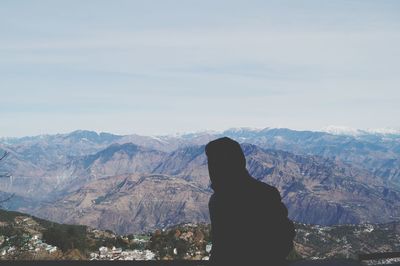 Man in hooded shirt standing on mountain against sky