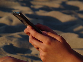 Close-up of hands using mobile phone at beach 