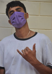 A young guy making shaka sign with his hand, wearing face mask with looking at camera