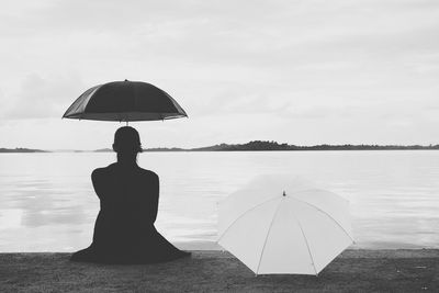 Rear view of silhouette woman with umbrella sitting at lakeshore