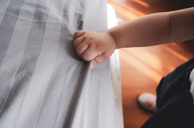 Cropped hand of baby girl holding bed sheet at home