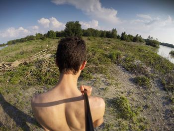 Rear view of shirtless man taking selfie on grassy field against sky