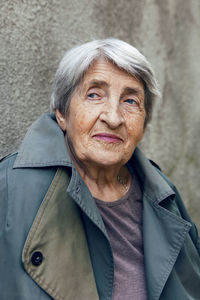 Portrait of an old siniors grandmother of 90 with gray hair stands against a gray wall on the street