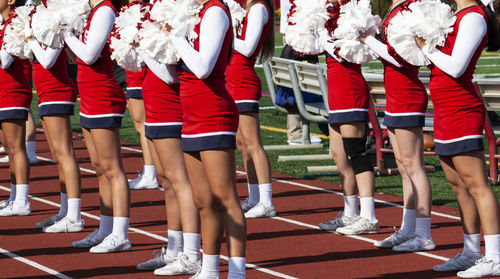High school cheerleaders in red and white uniforms cheer for fans at a high school football game.