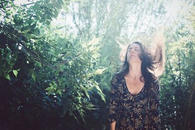 Woman tossing hair while standing against plants