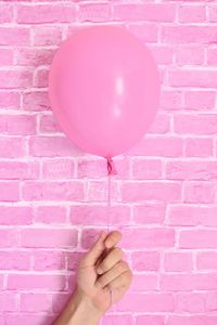 Cropped hand holding pink balloon against wall