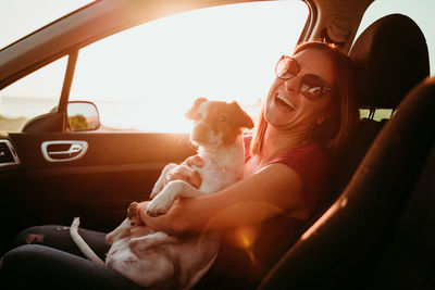 Portrait of smiling woman sitting in car with dog during sunset