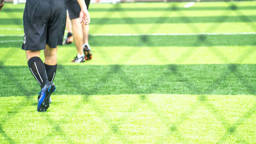 Low section of men playing soccer on field seen through chainlink fence