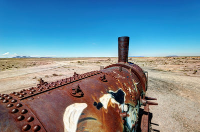 Old rusty metallic structure on field against clear blue sky