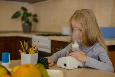 A sick child makes an inhalation with a nebulizer at home, he holds a mask from which steam 