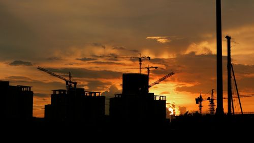 Silhouette of factory against cloudy sky during sunset