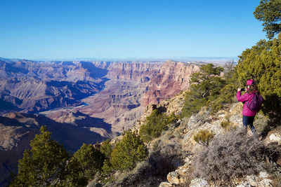 Woman taking photos with her mobile in the grand canyon national park. panoramic view.