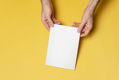 Low section of person holding paper against yellow background
