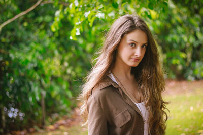 Portrait of beautiful young woman standing against trees