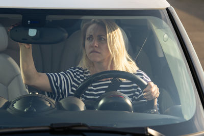 Mature woman adjusting mirror while sitting in car