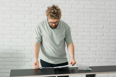 Side view of man using mobile phone while standing against wall