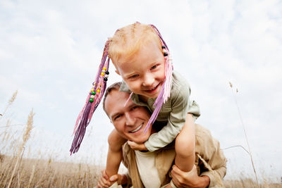 Close up optimistic portrait of happy red hair child sitting on shoulders father, smiling to camera