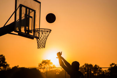 Silhouette man playing basketball against sky during sunset