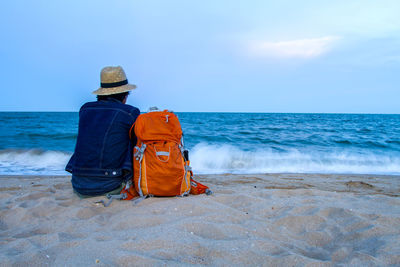 Rear view of man sitting at beach against sky