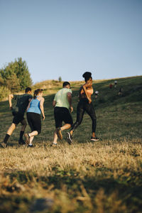 Rear view of male and female athletes running on grassy land