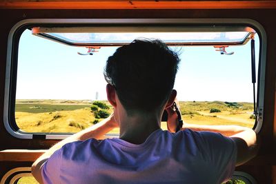 Rear view of man photographing through window in van