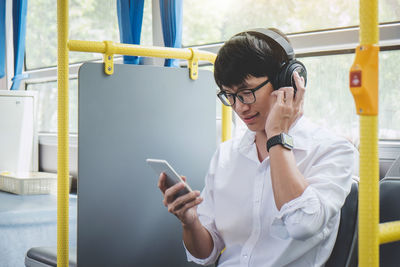 Young man listening music through headphones while using smart phone in bus