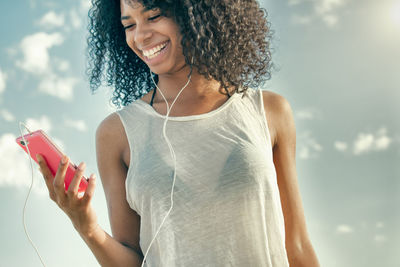 Young woman using mobile phone against sky