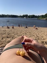 Low section of woman holding cherries on abdomen while lying at beach