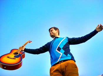 Low angle view of man holding guitar against clear blue sky