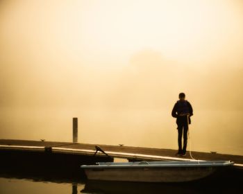 Man standing on pier over lake during sunset
