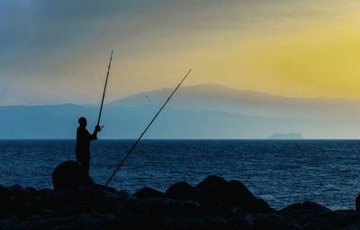 Silhouette man fishing by sea against sky during sunset