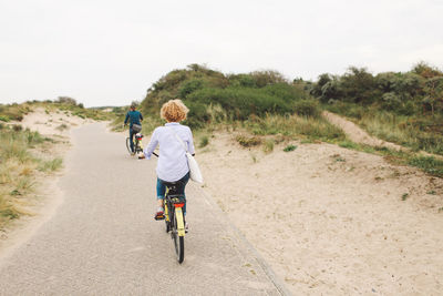 Rear view of friends riding bicycles on footpath at beach