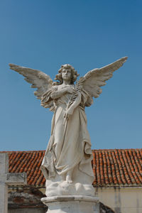 Cemetery statue. angel with wings. red tile roof in background.