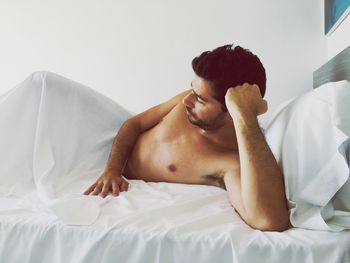 Shirtless mid adult man lying on bed against wall at home