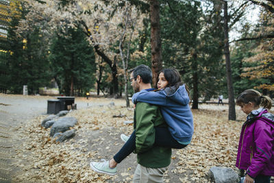 Side view of father piggybacking daughter while girl walking in forest at yosemite national park