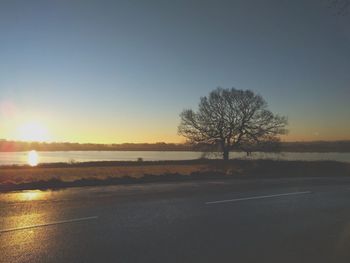 Road by trees against clear sky during sunset