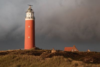 Lighthouse on field by building against sky