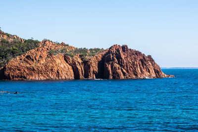 Rock formation in sea against clear blue sky