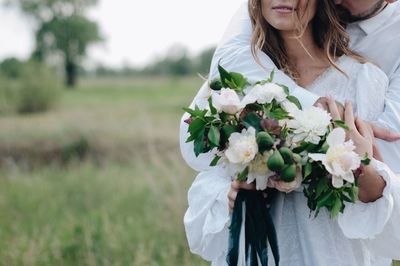 Cropped image of bridegroom embracing bride standing on field