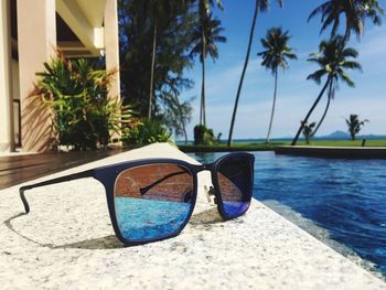 Close-up of sunglasses on poolside against blue sky during sunny day