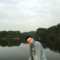 Portrait of young man by lake against cloudy sky