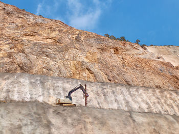 Man on rock by mountain against sky