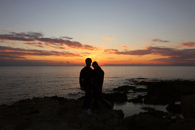 Silhouette couple standing at beach against sky during sunset