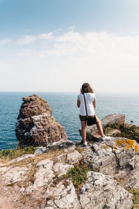 Rear view of woman standing on rock against sky