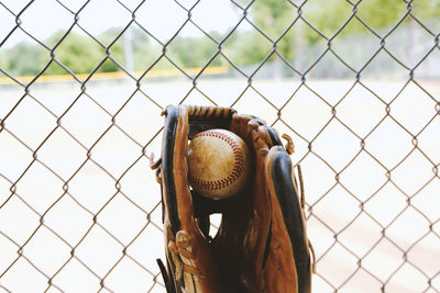 Close-up of baseball in glove against chainlink fence