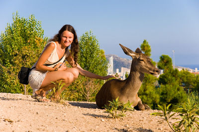 Full length portrait of woman sitting by deer on field 