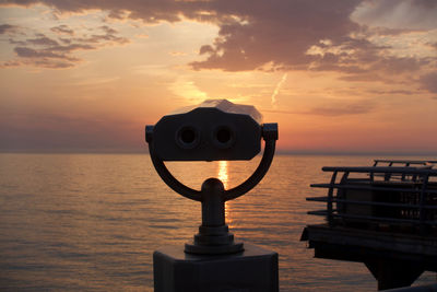 Coin-operated binoculars by sea against sky during sunset